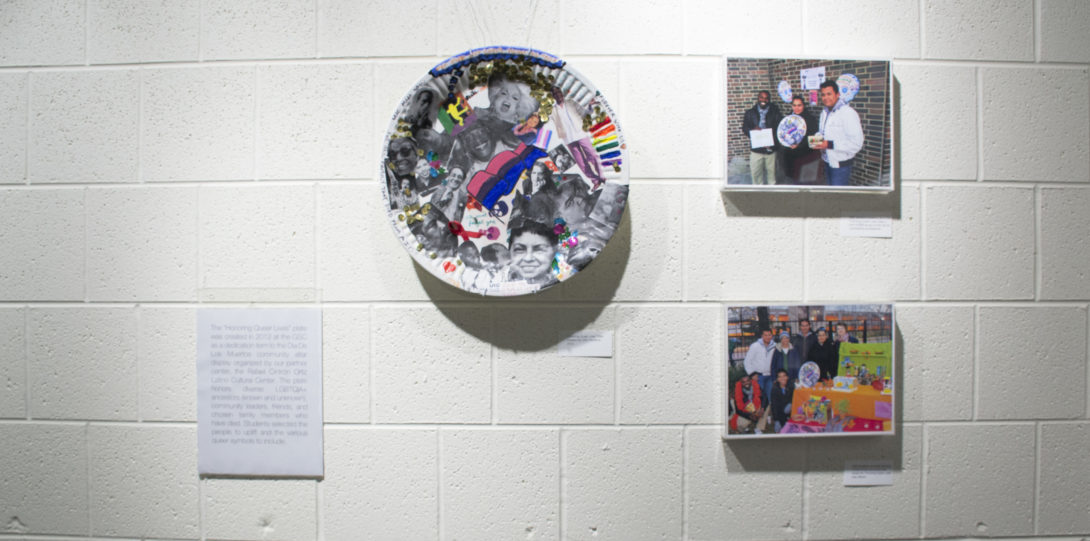 Photograph of the second half of the second wall. Showing a hanging plate and two photographs along with a label. The plate is decorated with a collage of materials.