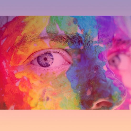Up close photograph of a person with rainbow paint over their face.