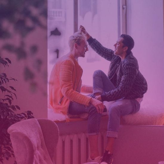 Photograph of two people sitting on a window ledge while laughing.