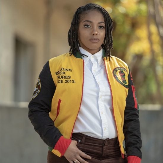 Janaé is in a yellow Jersey with black sleeves, a white button up shirt with a collar, and Maroon pants.