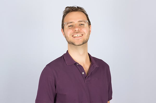 Nathan wearing glasses and smiling with a purple polo in front of a white background