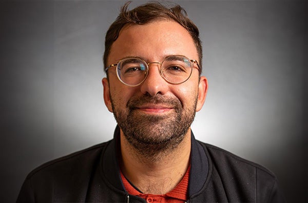 Jorge smiling wearing glasses with a red polo and black sweater in front of a black background.