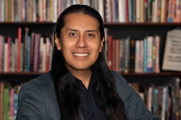 moises smiling wearing a blue blazer in front of books