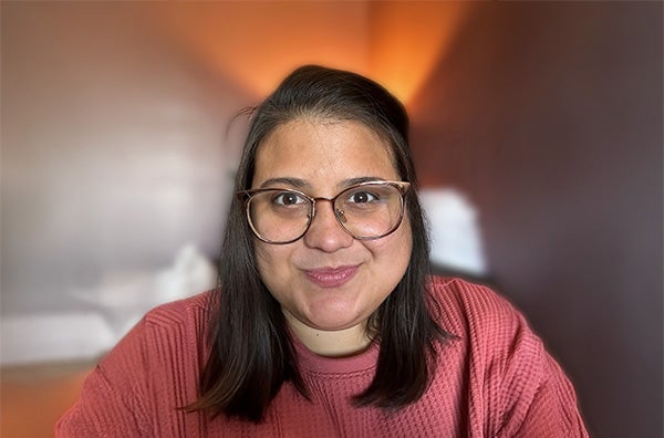 Olivia wearing glasses, pink sweater, long black hair, and smiling.